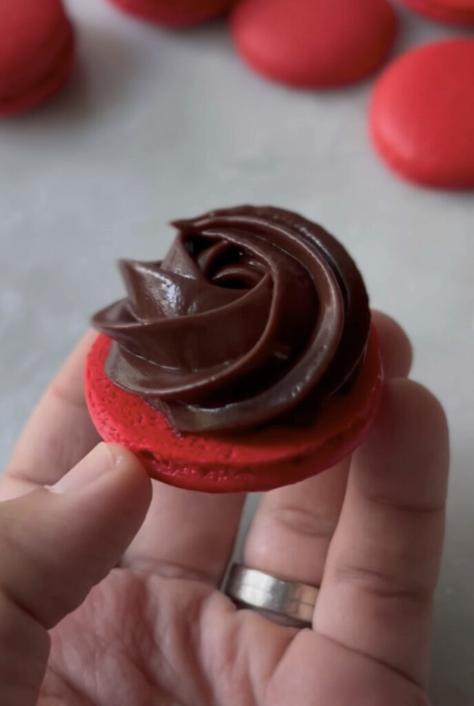 red macaron shell with chocolate ganache filling piped on top