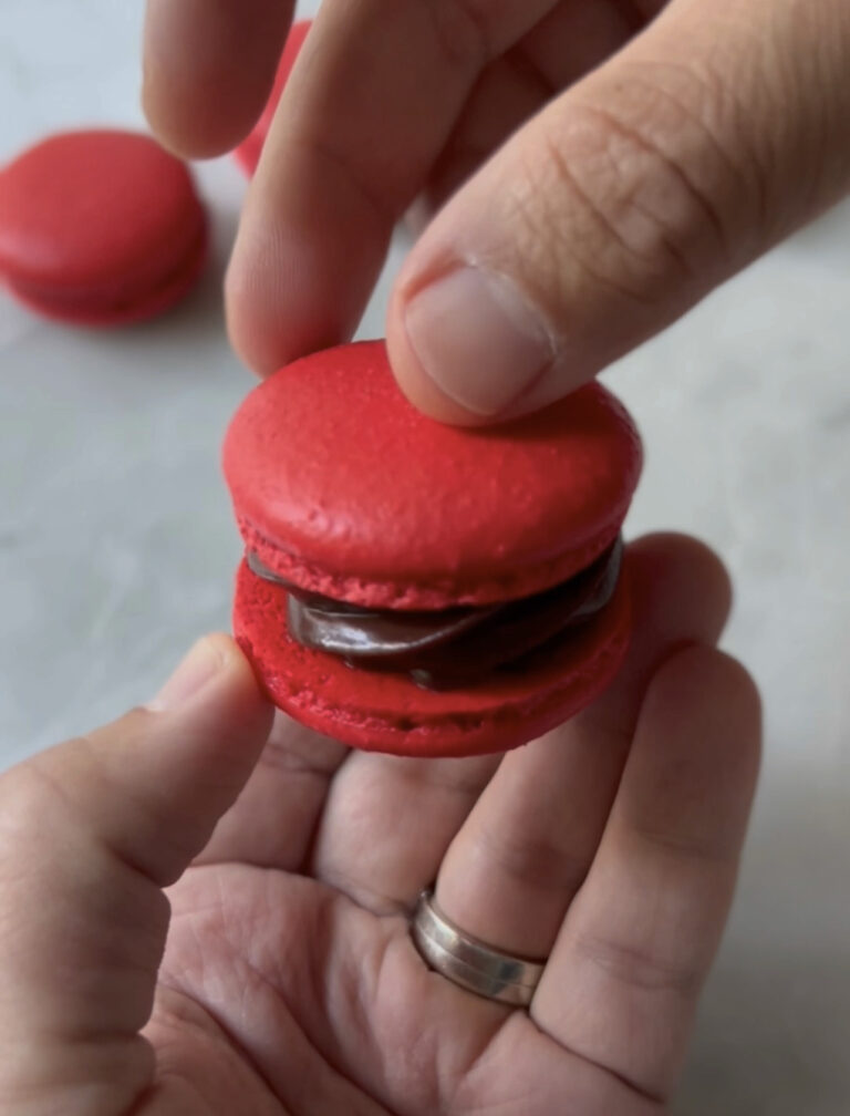 sandwiching a red macaron together with hands