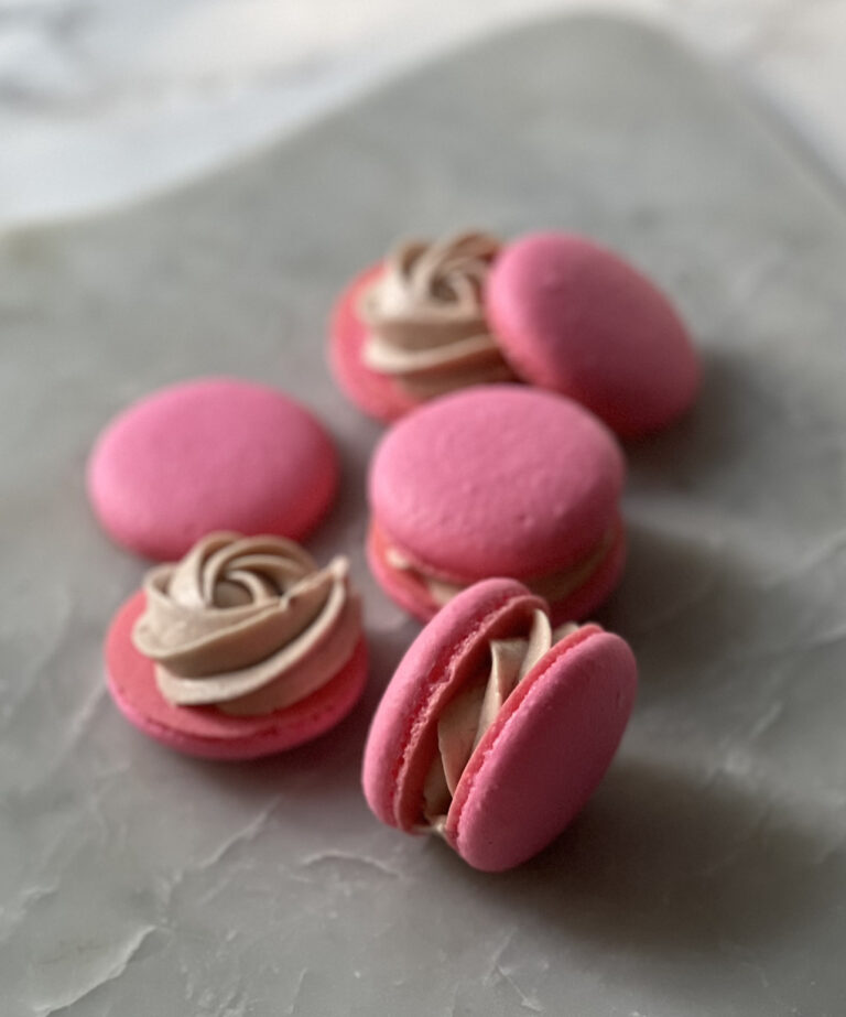 raspberry macarons with buttercream sitting on a slate counter