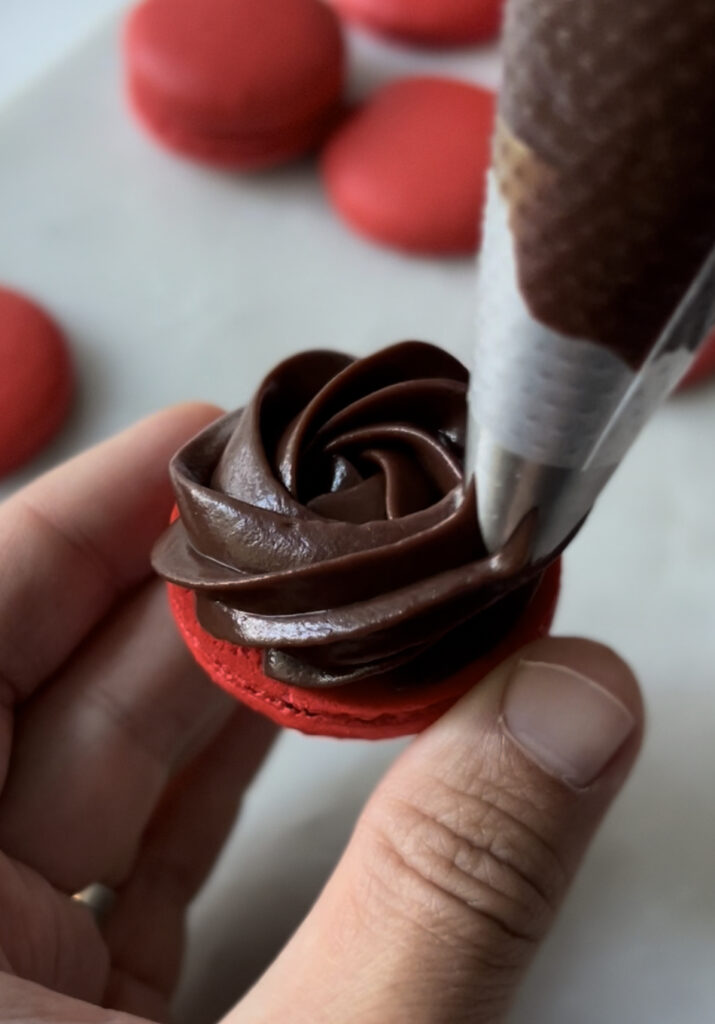 piping ganache on the shell of a macaron 